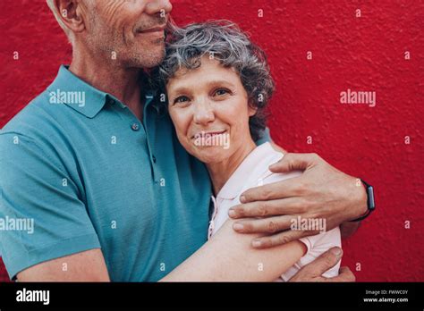 Portrait Of Happy Mature Woman Embracing Her Husband Against Red