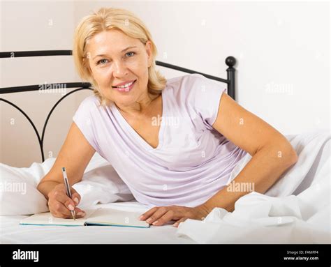 Blonde Mature Woman Writing In Diary And Laying In Bed At Home Stock