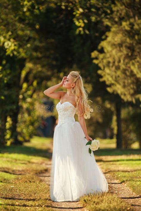 Retrato De Hermosa Novia Con Vestido De Novia Blanco Largo Con Ramo De Flores En El Parque