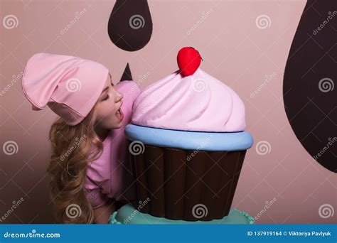 Hungry Blonde Woman Wearing Pink Cap Enjoying Big Cupcake At Studio