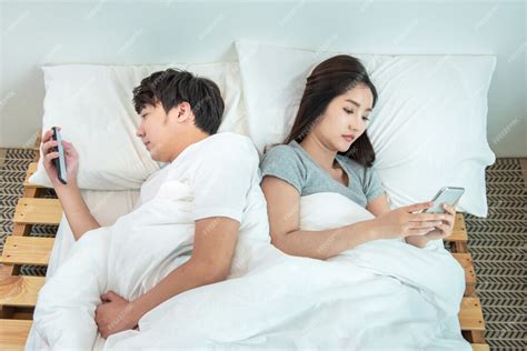 Premium Photo Young Asian Couple In Bed Using Phone Lying Backs To