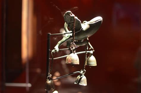 A Bird Figurine With Bells Hanging From It S Neck And On Display In A Glass Case