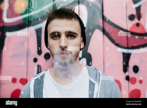 Young Man Standing In Front Of Graffiti Smoking Electronic Cigarette