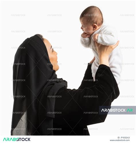 مفهوم الطفولة والأمومة ، بورتريه لأم عربية خليجية سعودية تحمل إبنها الرضيع بيديها لأعلى ، اللعب