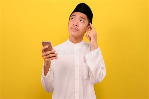 Young Asian Muslim Man Holding A Smartphone And Look Up Thinking An