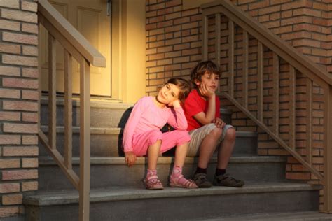 Brother And Sister Sit On Stairs Near Door At Evening Stock Photo