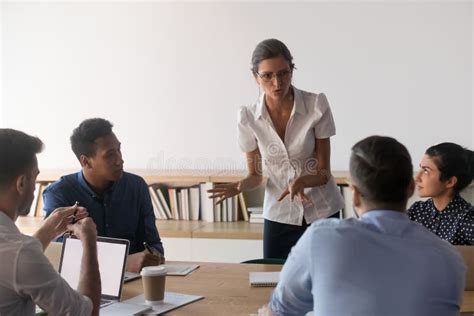 Serious Female Leader Talk To Diverse Employees Team At Meeting Stock