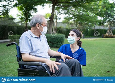 Asian Caregiver Wear Mask Take Care Senior Disabled Man On Wheelchair