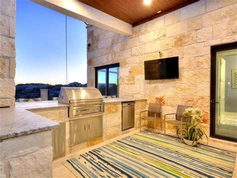 An Outdoor Kitchen With Grill Sink And Television On The Outside Wall