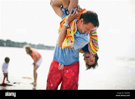 Father Carrying His Son Upside Down Over His Shoulder At The Beach