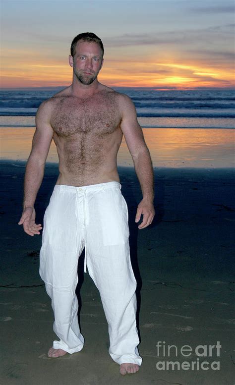Handsome And Sexy Hairy Man Stands On The Beach As The Sun Sets Behind