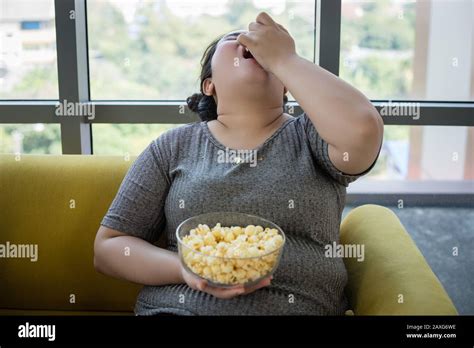 Overweight Woman And Asian Girl Enjoy Eating Food On Sofa At Home Stock