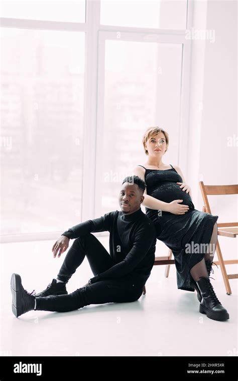 Young African Man And His Caucasian Pregnant Woman Sit On Chairs Interracial Marriage Concept