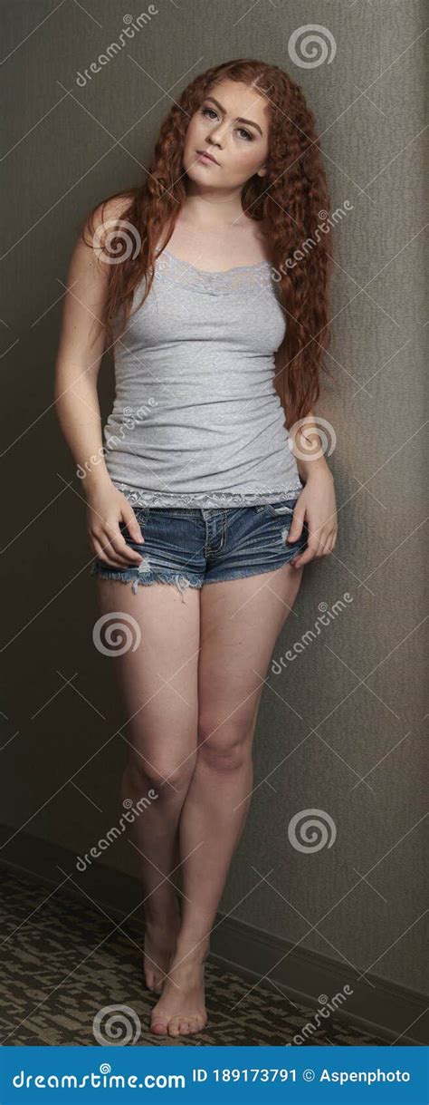 Young Redhead Woman Poses In Grey Tank Top And Denim Shorts Stock Image