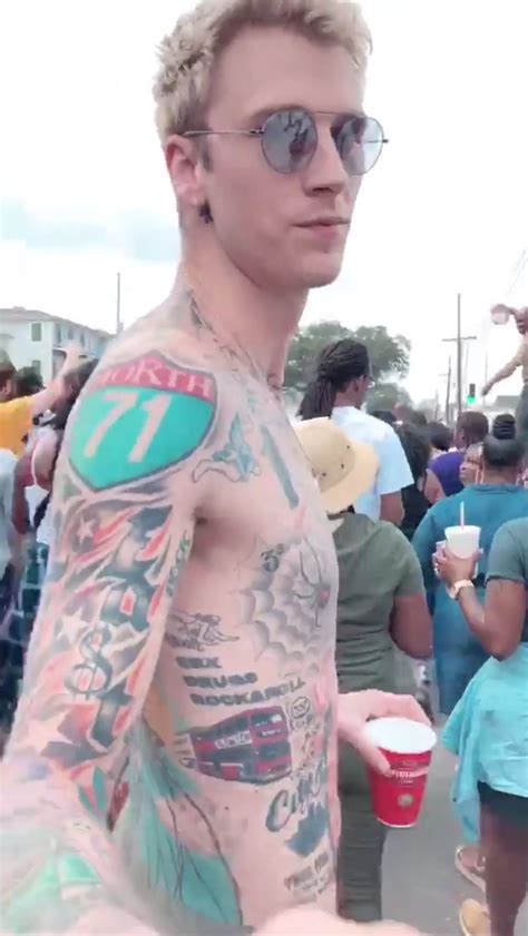 A Man With Tattoos On His Arm And Chest Standing In Front Of A Group Of