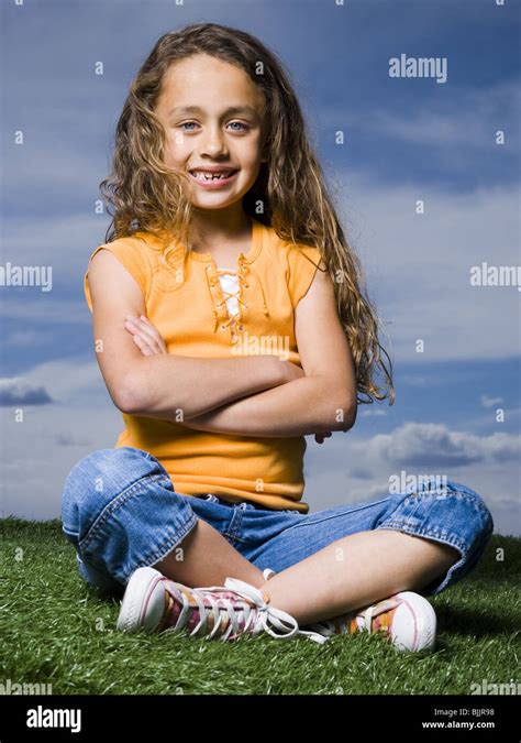 Girl Sitting Cross Legged On Grass Outdoors With Arms Crossed Smiling