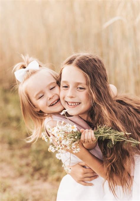 Two Little Girls Sisters Hug And Collect Flowers In The Summer Stock