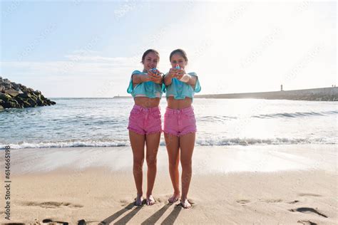 Twin Sisters In Matching Outfits Holding Squirt Guns On Beach At Sunny