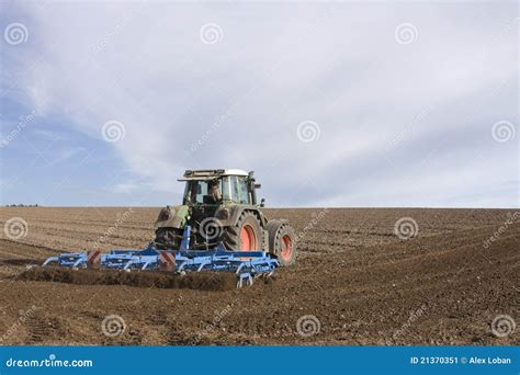 Tractor Ploughing Field With Blurry Farm In The Background Royalty Free