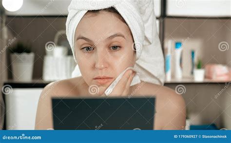 girl rubs her face attractive woman in bathroom with white towel on her hair looks in mirror