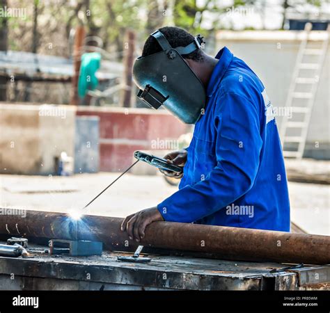 African Worker Welding Outdoors In The Factory Yard A Rusty Pipe