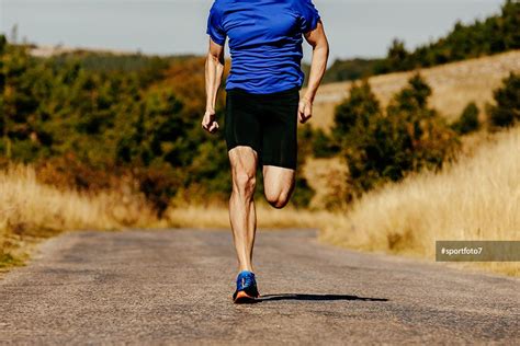 Muscular Legs Men Runner Running On Asphalt Road In Autumn Field