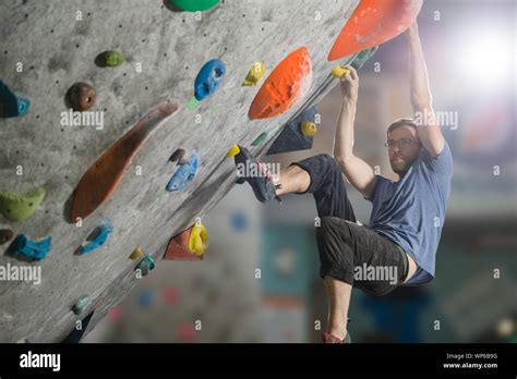 Young Active Sport Man With Beard And Glasses Climbing On Gym Wall