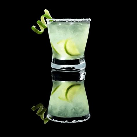 A Tall Glass Filled With Green Liquid And Lime Wedges On The Rim Next To A Black Background