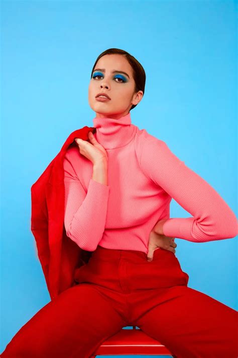 A Woman Sitting On Top Of A Wooden Bench Wearing Red Pants And A Pink Sweater