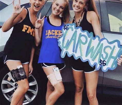 Three Girls Are Standing In Front Of A Car And Giving The Peace Sign With Their Hands