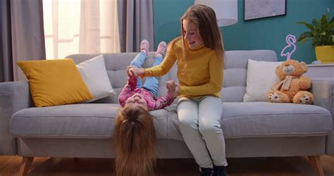 Two Caucasian Cute Sisters Playing Cheerfully On Sofa In Cozy Living