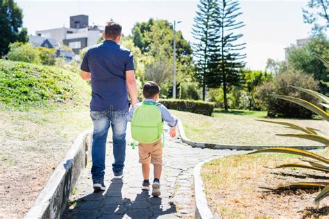 Padre Sosteniendo La Mano De Su Hijo Con Mochila Imagen De Archivo