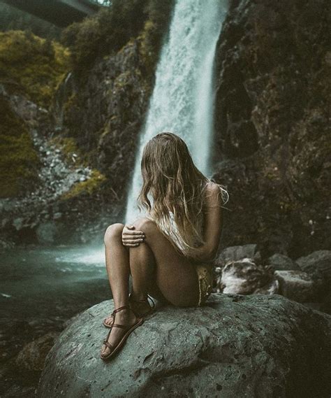 A Woman Sitting On Top Of A Rock Next To A Waterfall