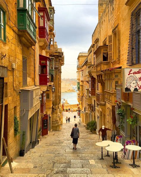 A Person Walking Down An Alley Way With Tables And Chairs