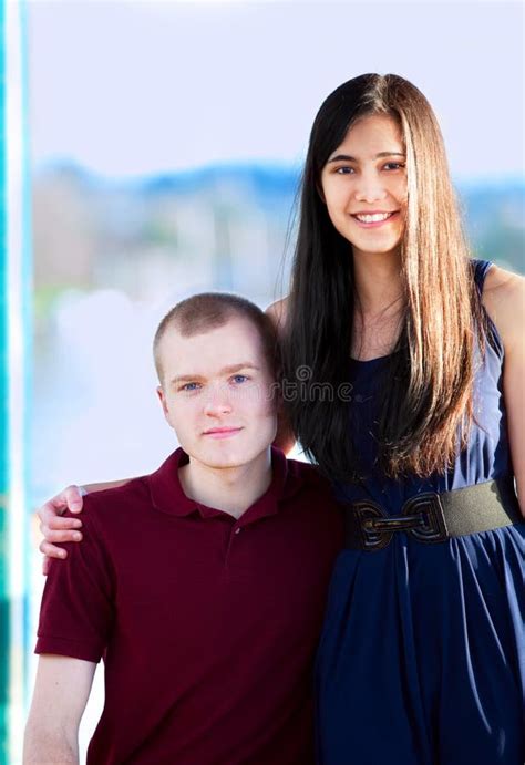 Young Woman Standing Next To Seated Young Man By A Lake Stock Photo