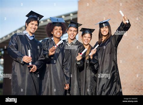 Students In Graduation Gowns Holding Diplomas On University Camp Stock