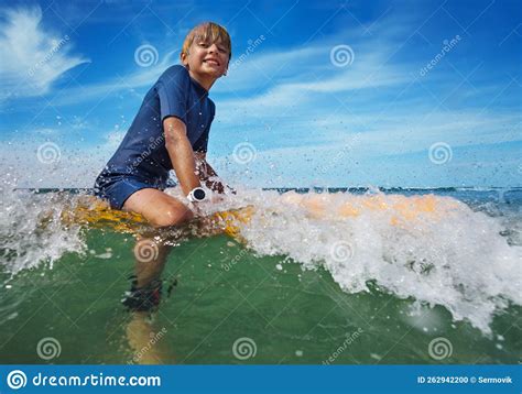 Low Angle Photo Of A Boy Sitting On The Surf Board In Waves Stock Photo