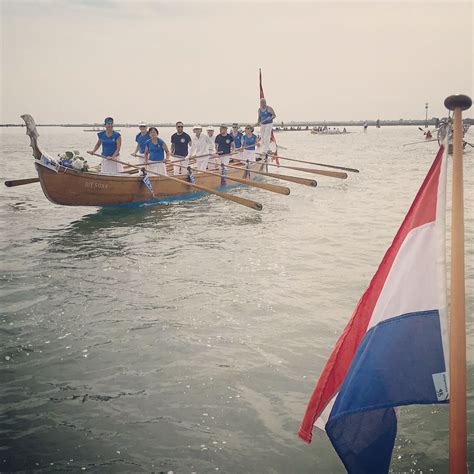 Two Long Boats With People On Them In The Water Next To A Flag And Pole