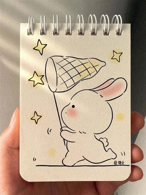 A Hand Holding A Notebook With A Drawing Of A Rabbit On It