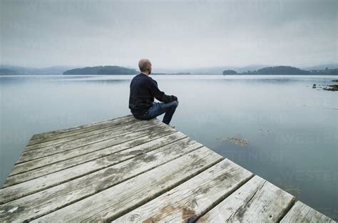 Lonely Man Sitting On Jetty Looking At Distance Stock Photo