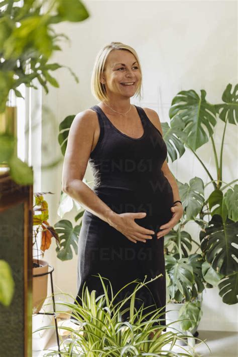 Happy Mature Pregnant Woman Standing Between Leaves In Living Room