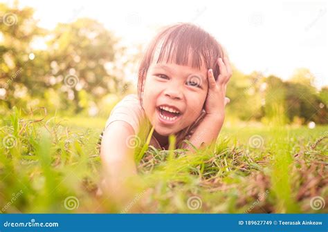 Happy Little Child Girl Lying On Green Grass Outdoors In Summer Park