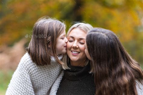 Two Happy Girls Daughters Kissing Their Mother In The Cheeks Stock