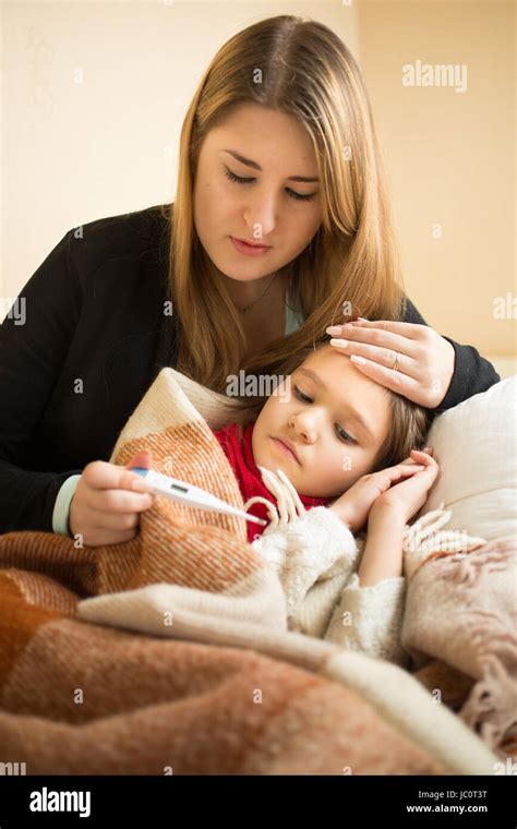 portrait of caring mother measuring sick daughter temperature with digital thermometer stock