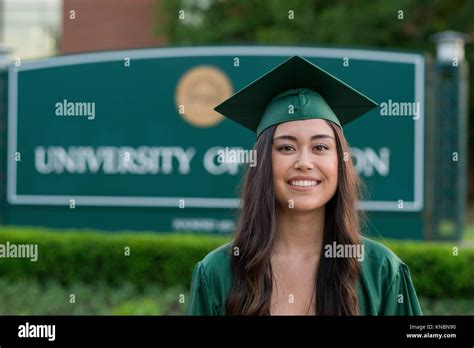 Female Graduating Student In Her Cap And Gown With A Blurred Out College School Sign In The