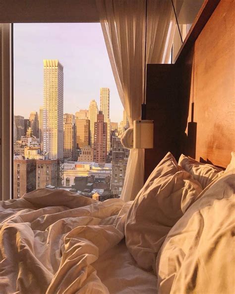An Unmade Bed In Front Of A Large Window With Cityscape Behind It