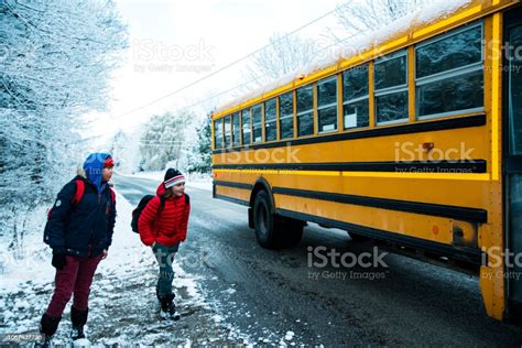 Two Children Getting On A School Bus On A Cold Snowy Winter Morning In