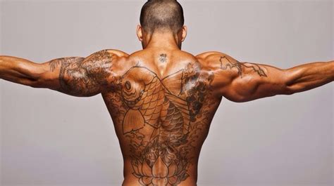 The Back Of A Man With Tattoos On His Upper And Lower Body Showing Muscles