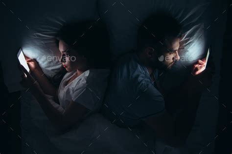Couple Lying Back To Back In Bed And Using Smartphones At Night Stock