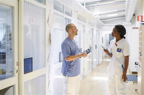 Male And Female Nurse Discussing While Standing In Corridor At Hospital